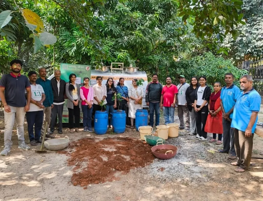Group of volunteers standing behind blue drums, buckets and a heap of red soil prepared for planting saplings