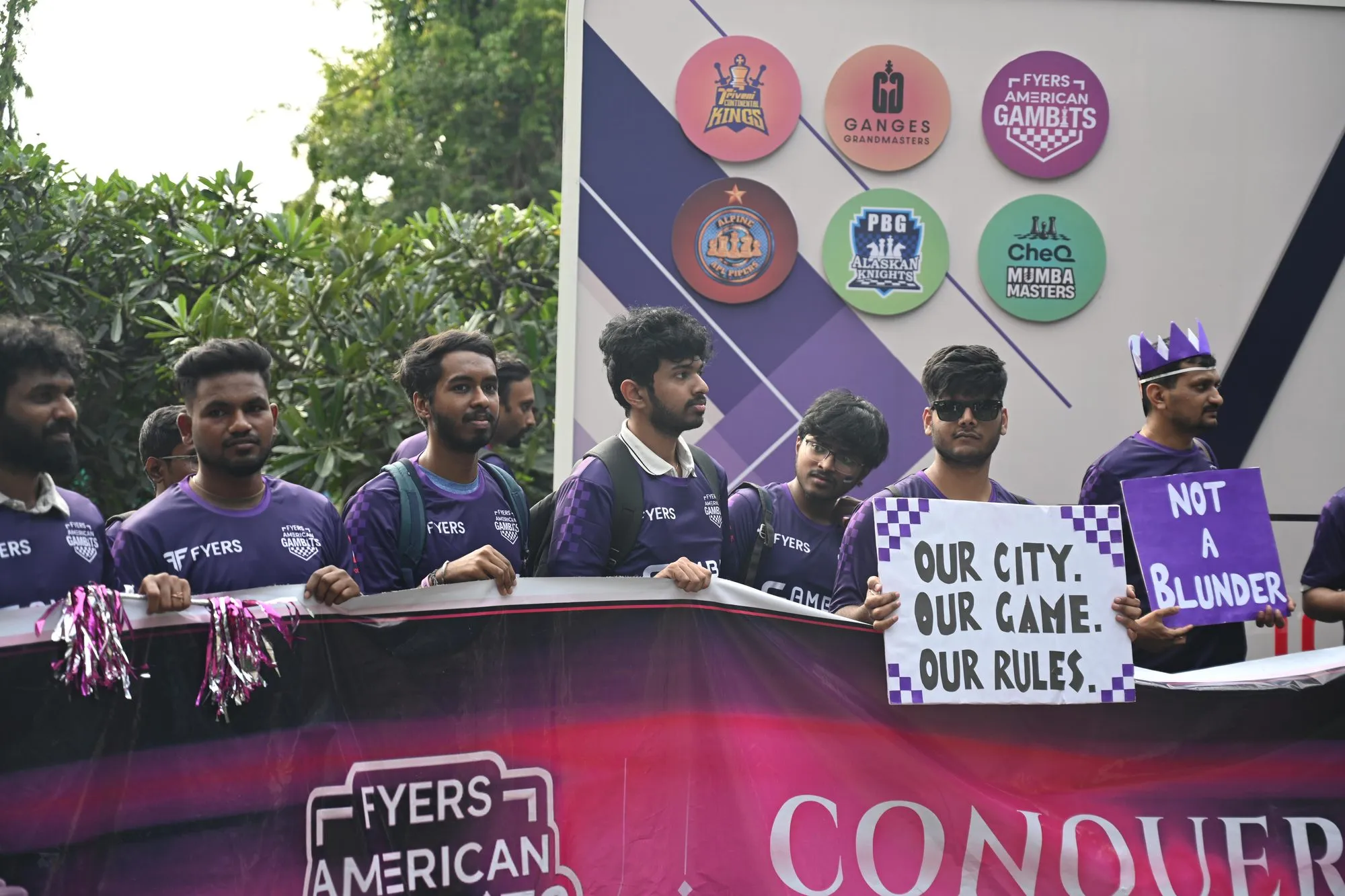 The Gambits Gang in purple jerseys behind the American Gambits banner at the Global Chess League, holding hand-made signs
