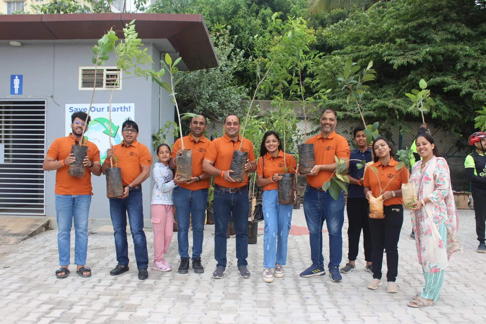 Volunteers in matching orange T-shirts holding saplings in grow bags before a tree-planting drive